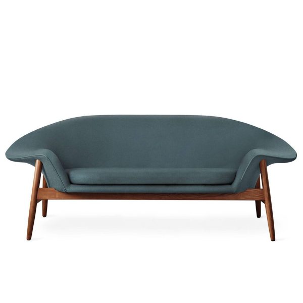 En moderne blågrøn sofa med glat, buet ryg og slanke træben. Sofaens design har et minimalistisk look med et dybt, polstret sæde.