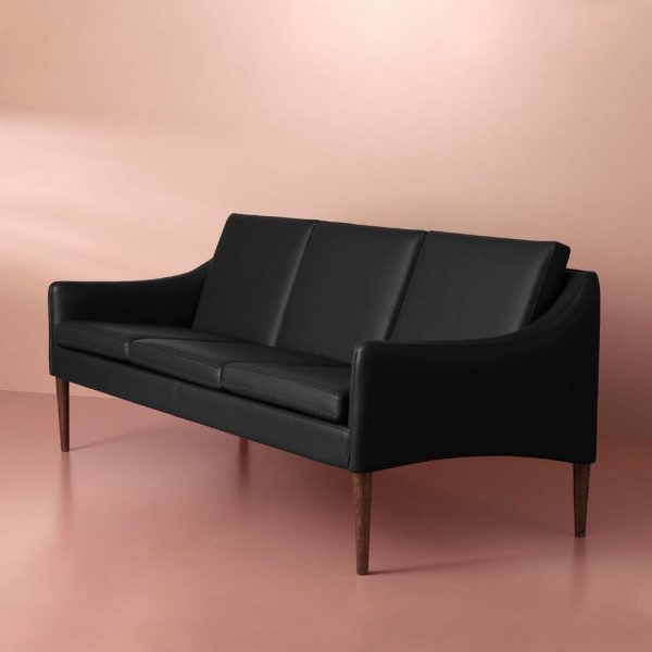 En elegant sort lædersofa med et minimalistisk design, sat mod en blød pink baggrund. Sofaen har tilspidsede træben og et let buet ryglæn, der perfekt fanger essensen af moderne interiørdesign.