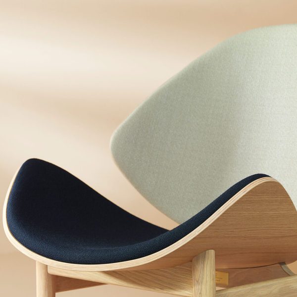 Nærbillede af en moderne designmøbler stol med lys træramme og kontrasterende mørkeblå og lys beige polstret sæde og ryglæn. Baggrunden er en blød, neutral tone.