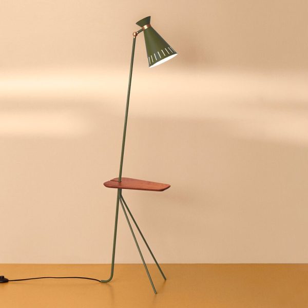 En moderne gulvlampe med en grøn metalramme og en rund træhylde, med en konisk skærm, står op ad en almindelig lysebrun væg på matchende designmøbler.