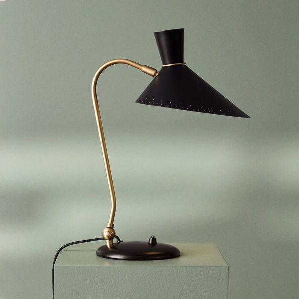 En stilfuld bordlampe med en lækker sort skærm og en buet gylden arm fra TomorrowsDesign står på en mørk overflade mod en blød grøn baggrund.