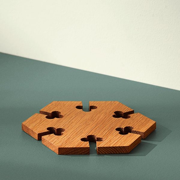 En træpuslespilsbrik med en manglende midtersektion sidder på en grøn overflade mod en beige væg og kaster en defineret skygge. Træets tekstur er tydeligt synlig, hvilket afspejler dets udsøgte design.