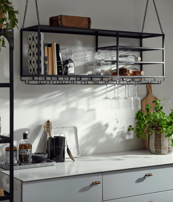 Et stilfuldt køkkeninteriør med en hængende hylde med bøger, glas og redskaber over en hvid bordplade med dekorative planter og en NORDAL - Marbi Vinkøler.