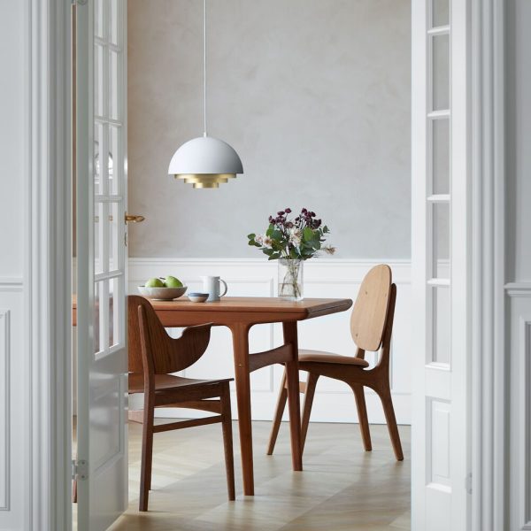 En lys, minimalistisk spisestue med et træbord med matchende møbler, en skål med grønne æbler, en vase med lilla blomster og en hvid pendel. Hvide døre er lidt åbne i forgrunden.