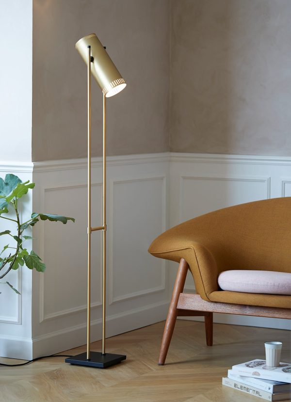 En slank, moderne gulvlampe med metallisk finish står ved siden af en elegant moderne sofa fra midten af århundredet i et rum med klassiske wainscoting og en lille potteplante. Rammerne viser smukt skandinavisk designmøbler.