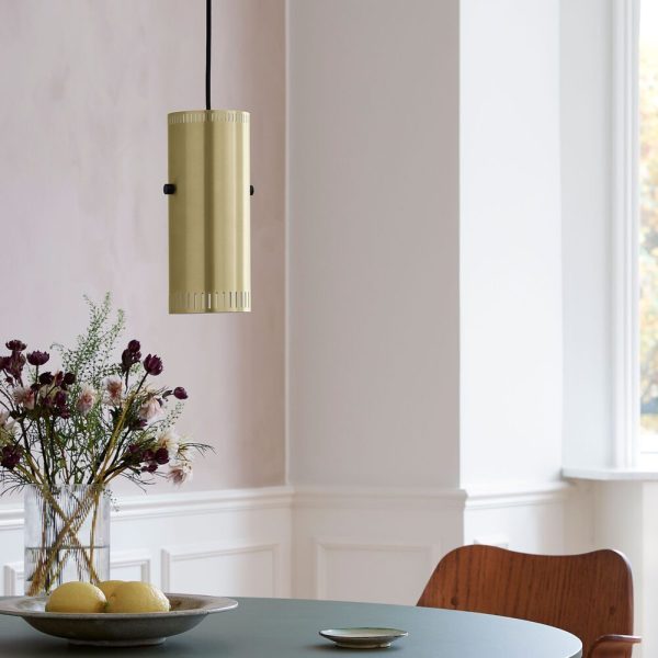 En stilfuld spisestue med en moderne guldpendel hængende over et rundt grønt bord prydet med en skål med citroner og en vase med blomster. Værelset byder på klassiske hvide paneler, store vinduer og skandinaviske interiørdesignelementer.