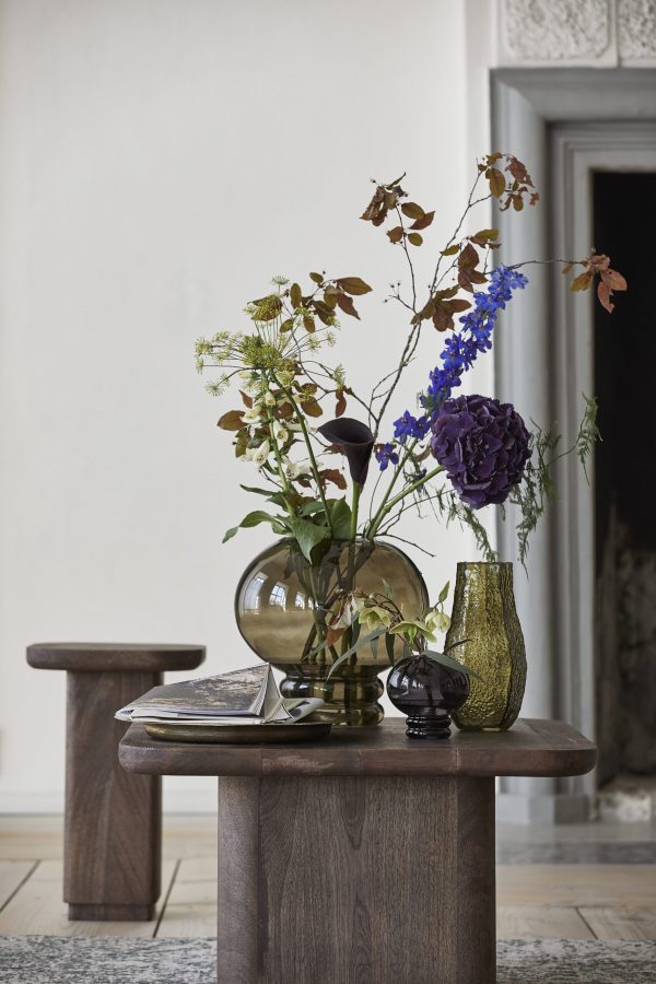 Et rustikt træbord med en række vaser indeholdende farverige blomster, herunder blå delphiniums og en lilla hortensia, parret med en bog og dekorative genstande i et elegant rum designet af TomorrowsDesign.