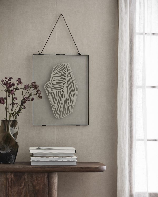 Et minimalistisk opholdsrum med en indrammet abstrakt hvid skulptur hængende på en tekstureret beige væg ved siden af et rent hvidt gardin. Et konsolbord af træ rummer en vase med lilla blomster og en stak bøger, der perfekt inkarnerer essensen af TomorrowsDesign.