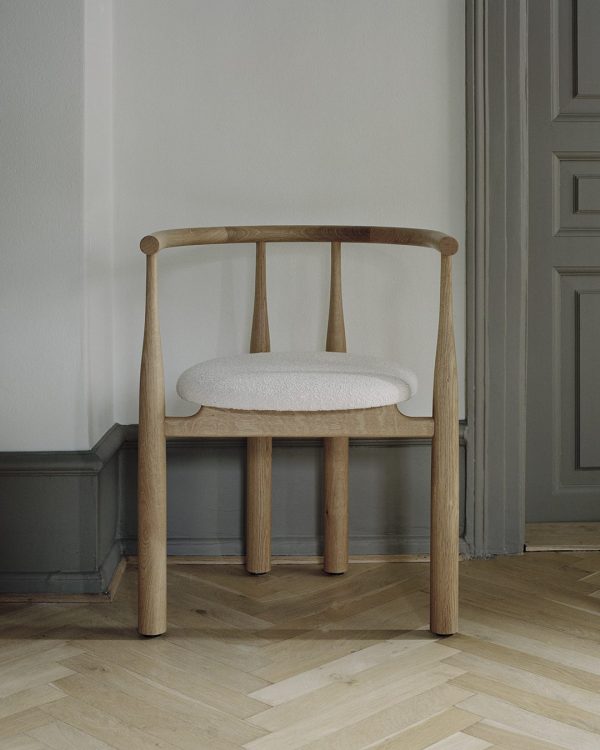 En træstol med buet ryglæn og en tekstureret hvid sædehynde, designet til komfort og stil, stående på et sildebensmønstret trægulv mod en almindelig væg med en lukket grå dør.