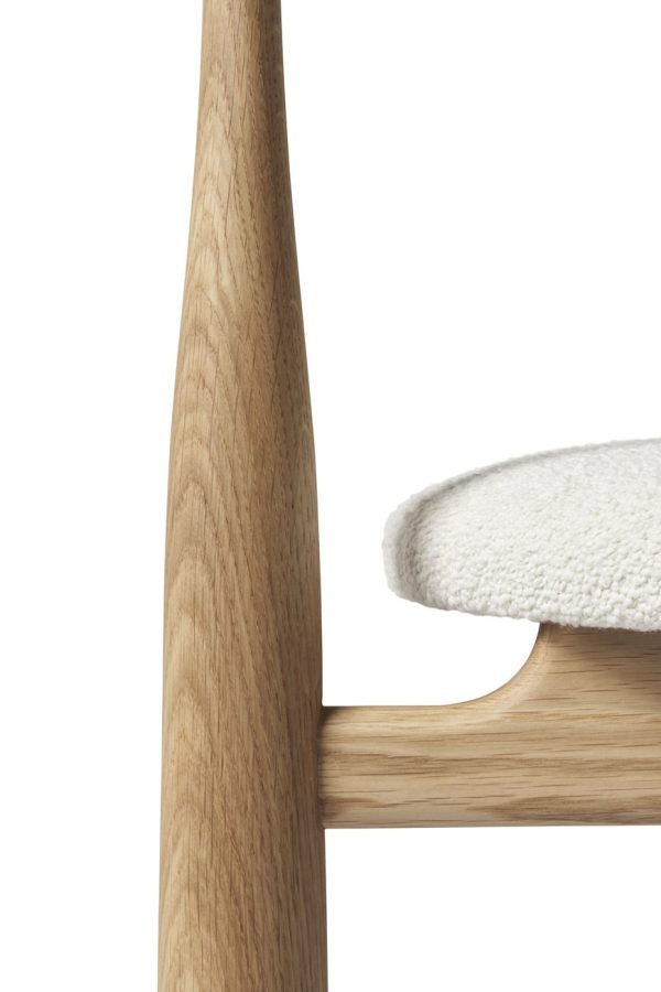 Nærbillede af en moderne stol, der viser dens træramme og hvide pude med fokus på håndværket og detaljerne i træets struktur, perfekt til TomorrowsDesign.