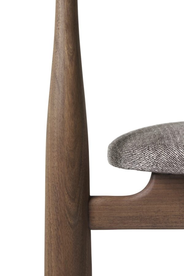 Nærbillede af en moderne stol med en glat træramme og en tekstureret grå stofpude, vist mod en hvid baggrund. Fokus på armlænet og en del af sædet fanger dets elegante design.