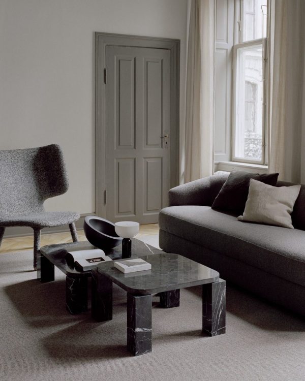 Interiør i en minimalistisk stue med en grå sofa, en tekstureret lænestol og et marmor sofabord fra TomorrowsDesign. Indeholder neutrale toner, stort vindue med gardiner og en lukket dør.