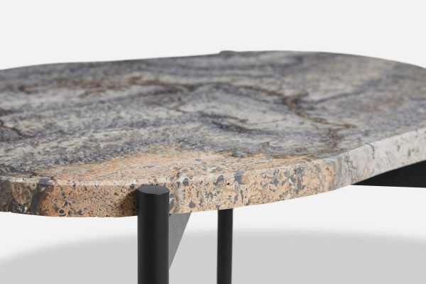 Nærbillede af et rundt bord med en struktureret, plettet stenoverflade og sorte metalben, designet som moderne møbler, isoleret mod en hvid baggrund.