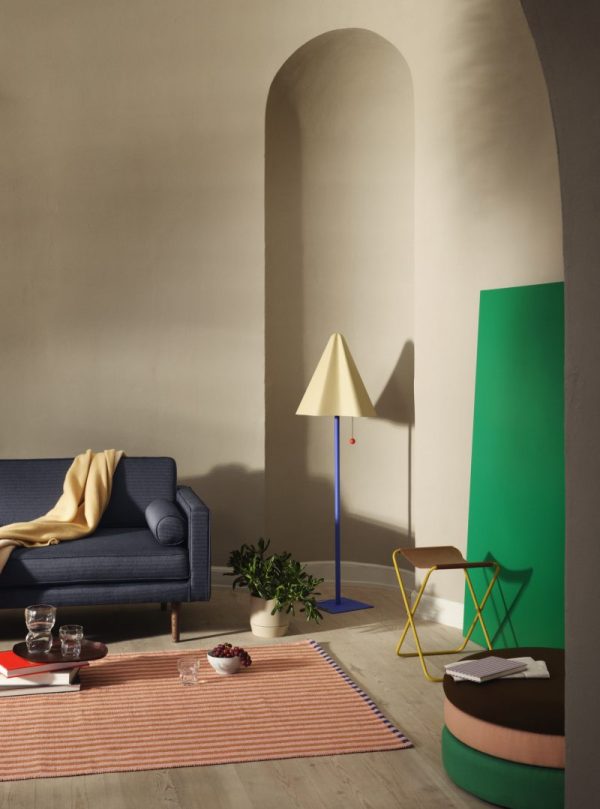 Stilfuldt stuehjørne med BROSTE COPENHAGEN - 'Wind' Sofa 2-Personers, sennepskast, stribet tæppe og unik lampe ved siden af et grønt panel og buet døråbning. et geometrisk sidebord med bøger og en kaffekop tilføjer et moderne touch.