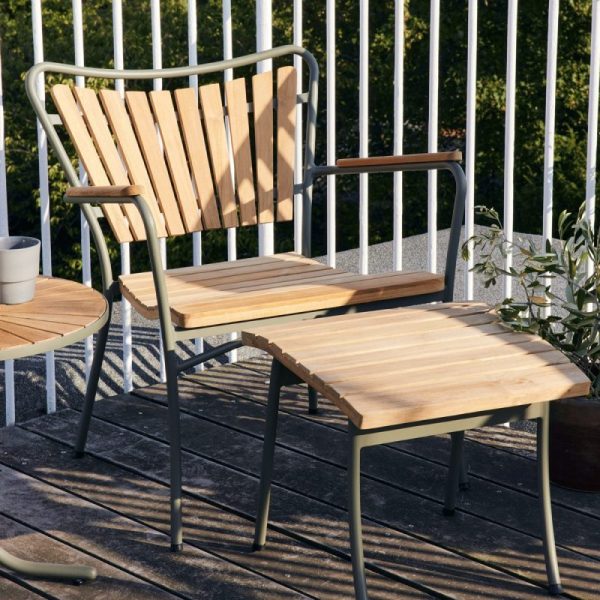 En træstol med armlæn og et matchende lille bord på en udendørs balkon, oplyst af sollys. Indstillingen omfatter grønne potteplanter, hvilket antyder et roligt, afslappet miljø designet af TomorrowsDesign.