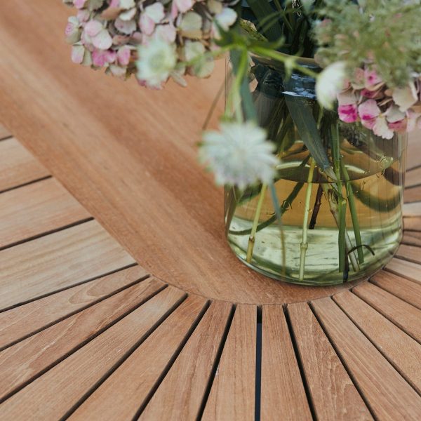 En klar glasvase med flere afskårne blomster, primært lyserøde og grønne, reflekteret i et rundt spejl placeret på et trælamelbord fra TomorrowsDesign.