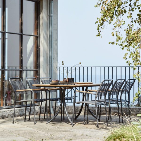 Udendørs spiseplads med et træbord og seks metalstole på en terrasse med store glasvinduer og udsigt til et diset sølandskab i baggrunden. Arrangementet inkluderer designermøbler for forbedret æstetisk appel.