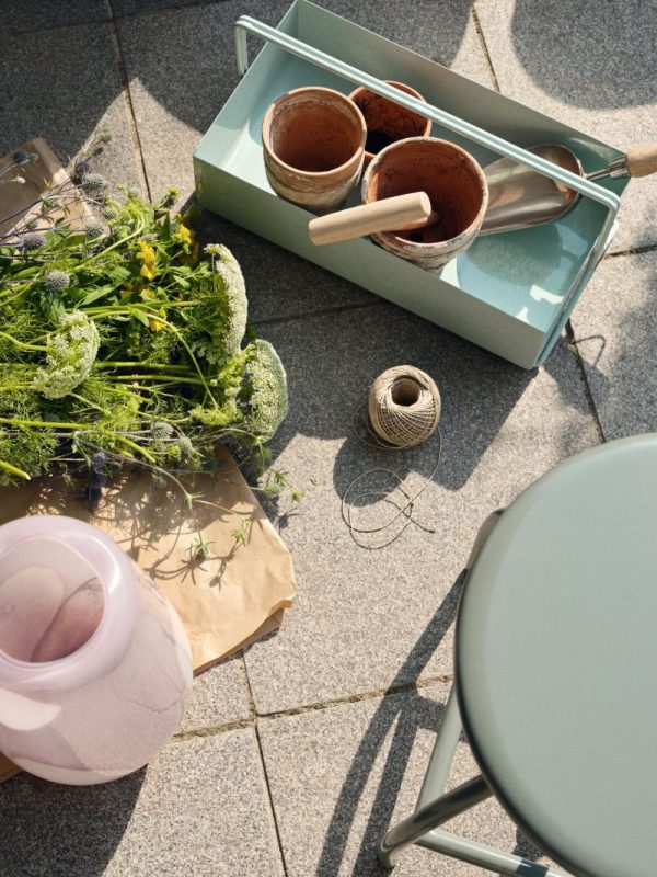 Set ovenfra af en havescene med en bakke med potter og værktøj, en kugle sejlgarn, friske afskårne blomster og en lyserød vandkande på et klinkegulv ved siden af en BROSTE COPENHAGEN - 'Sire' Barstol.