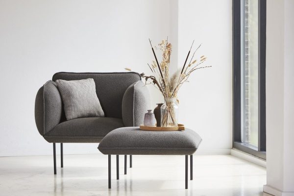 EN WOUD - Nakki Lænestol lænestol med hynder ved siden af et vindue i et lyst, minimalistisk rum. en træbakke med en vase med tørrede planter sidder på stolen.