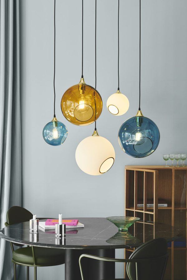 Moderne spisestue med et marmorbord med grønne stole og DESIGN BY US - Ballroom Lampe hængende ovenover. et træskab og blå gardiner er synlige i baggrunden.