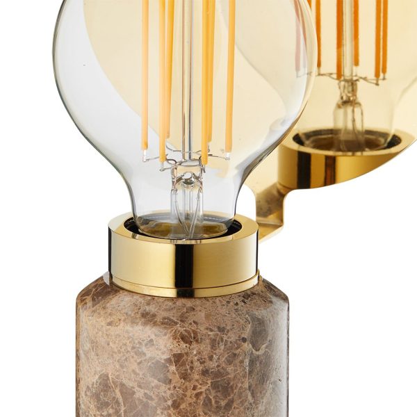 Nærbillede af et DESIGN BY US - Blindspot Bordlampe med en klar, kugleformet led-pære monteret på en messingfatning, som er fastgjort til en grå, marmoreret stenfod. baggrunden inkluderer et spejl, der reflekterer pæren.