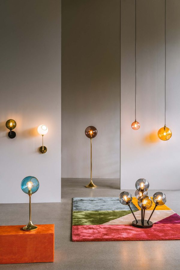 Moderne showroom med en kollektion af DESIGN BY US - Ballroom-lamper med forskellige designs, sat mod et minimalistisk interiør. Lamper har sfæriske og cirkulære former på podier og vægge, fremhævet under blød belysning.