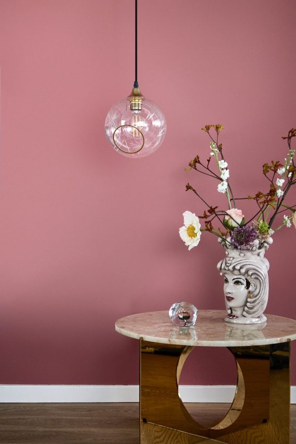 Et stilfuldt interiør med et rundt marmorbord mod en lyserød væg, prydet med en klassisk bustevase fyldt med blomster. Over bordet hænger en DESIGN BY US - Ballroom Lampe Diamond Cut pendel.