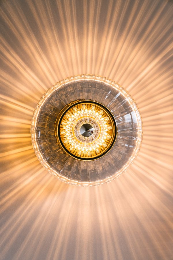 Et nærbillede af et DESIGN BY US - New Wave Optic Væglampe loftsarmatur fra direkte neden, der viser indviklet glasdesign og symmetriske lysstråler, der stråler udad.