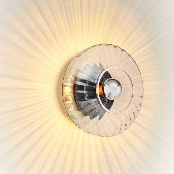 Et nærbillede af en DESIGN BY US - New Wave Optic Væglampe med et tydeligt solstrålemønster og synlig pære, der udsender en varm glød.
