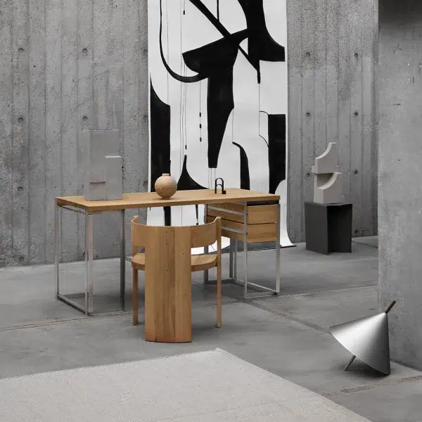 Et moderne minimalistisk kontor med et træskrivebord, en stol og abstrakt sort/hvid kunst på betonvægge. En metallisk lampe vipper på gulvet nær en simpel TomorrowsDesign-hylde.
