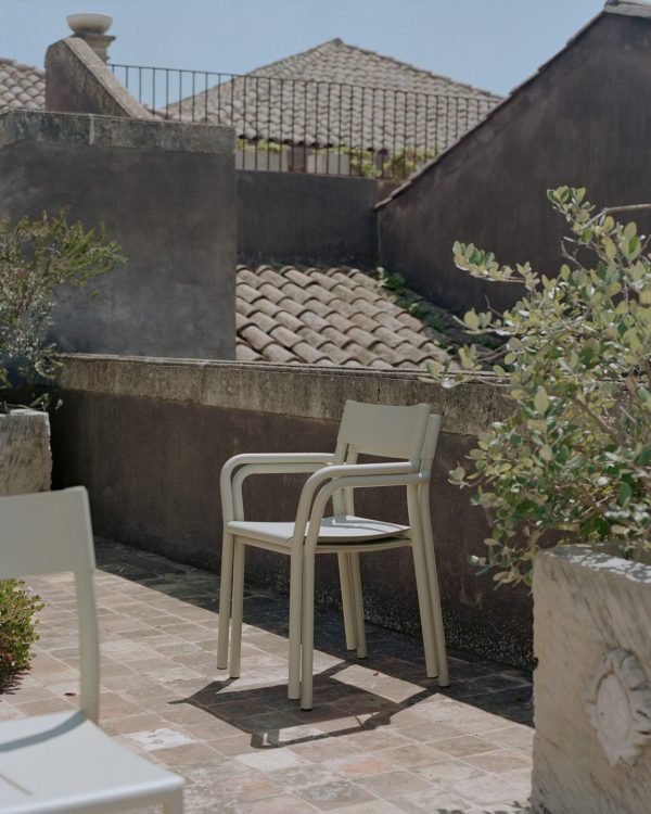 ET NYT VÆRK - May Havestol på en flisebelagt terrasse, omgivet af rustikke stenvægge og terracotta tagsten, med udsigt til solrige middelhavsomgivelser.