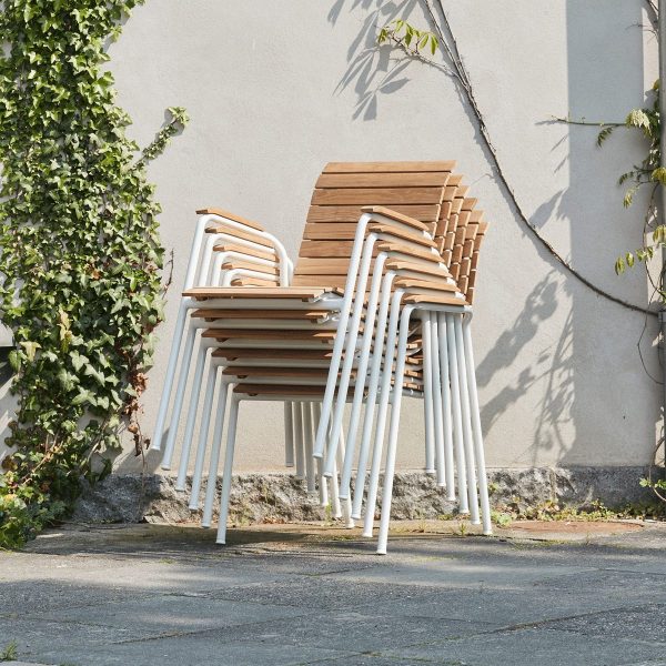 En stak MANDALAY - Bellevue & Magnolia Havesæt med hvide metalben, med TomorrowsDesign, pænt arrangeret mod en grå betonvæg, delvist skygget af grøn efeu.