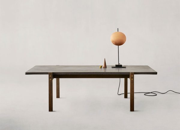 Et minimalistisk setup med en EBERHART - Eugene Sofabord med en sfærisk ferskenfarvet lampe og en lille kegleformet genstand på den, sat mod en lysegrå baggrund.