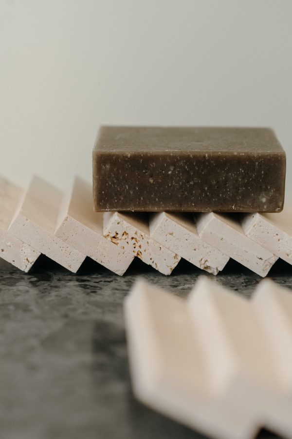 Et stykke brun sæbe sidder oven på flere vinklede hvide WABI SABI NORDIC - Sæberist med en kontrasterende mørkegrå baggrund, der fremhæver en forenklet og ren designæstetik.