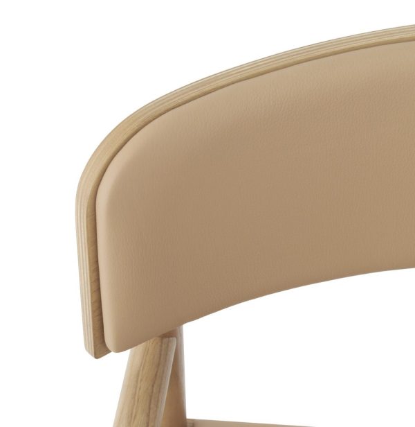 Nærbillede af en stoleryg, der viser et beige læderbetræk og en lys træramme på en isoleret hvid baggrund, perfekt til indretningstemaer.