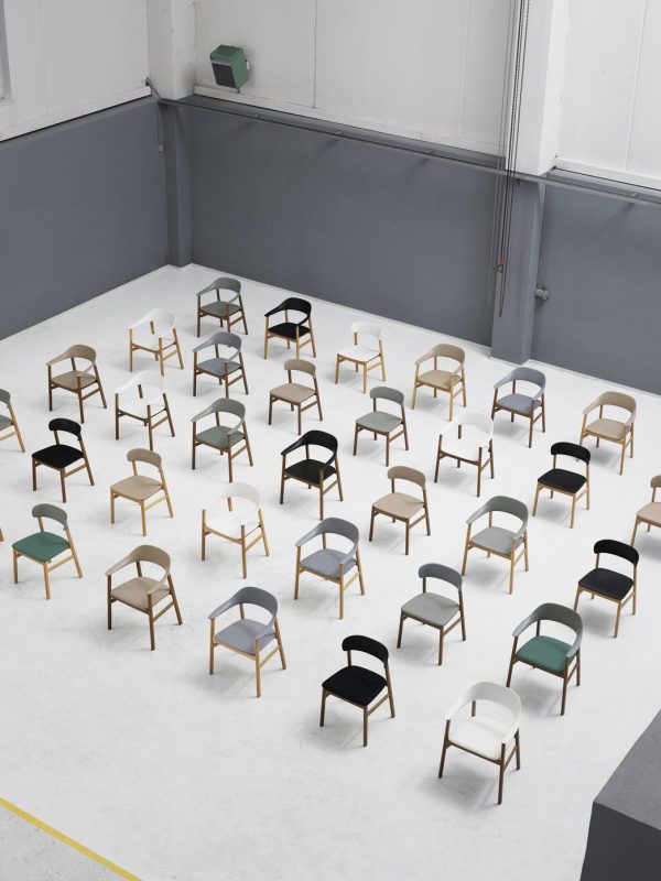 Et sortiment af moderne designmøbler arrangeret i rækker på et gråt gulv i et rum i industriel stil, med kombinationer af forskellige farver og materialer synlige.