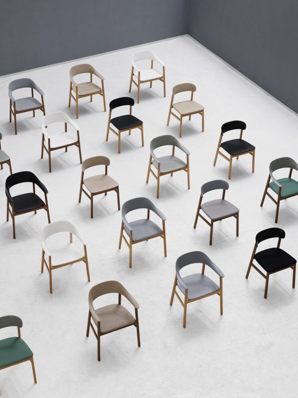 En række moderne designmøbler stole med træstel og stofsæder, arrangeret i et organiseret mønster på et gråt gulv mod en grå væg, med forskellige farver som tan, hvid, grøn og sort.