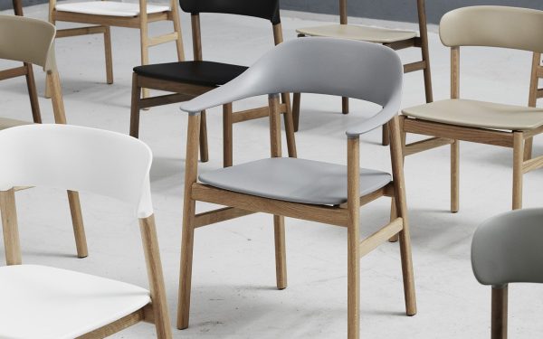 En kollektion af moderne designmøbler med træben og slanke plastiksæder i forskellige farver, arrangeret på et betongulv i et rummeligt, godt oplyst rum.