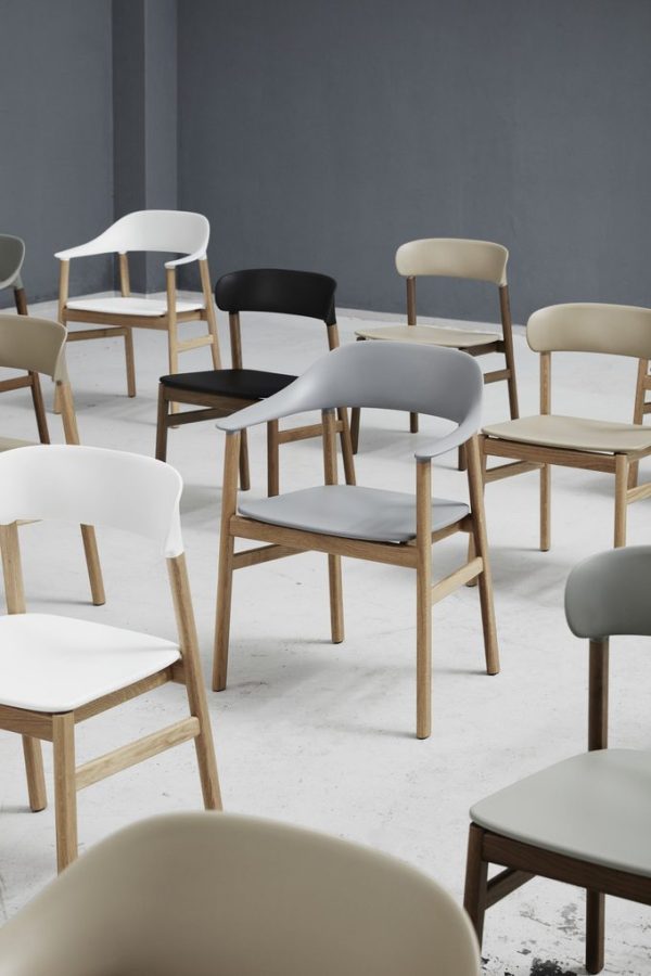 Flere NORMANN COPENHAGEN - Herit Spisebordsstol stole med træben og plastsæder i forskellige farver, herunder hvid, sort og grå, tilfældigt anbragt på et betongulv mod en grå væg.