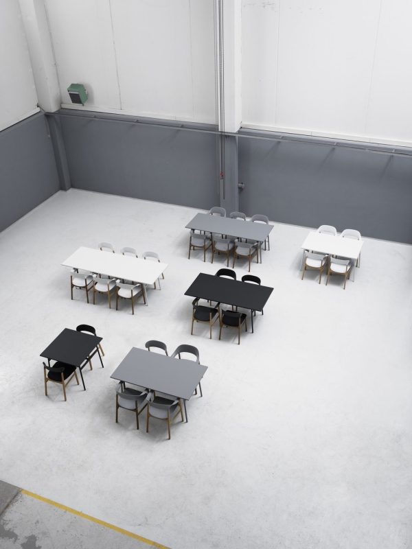 Luftfoto af et sparsomt møbleret værelse med flere sorte og hvide designborde parret med stole. Betongulvet og de grå vægge bidrager til et minimalistisk, moderne udseende.