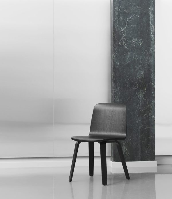 Et minimalistisk interiør med en elegant sort stol placeret ved siden af en mørk marmorsøjle mod en hvid væg. Scenen formidler en moderne, ren designæstetik.