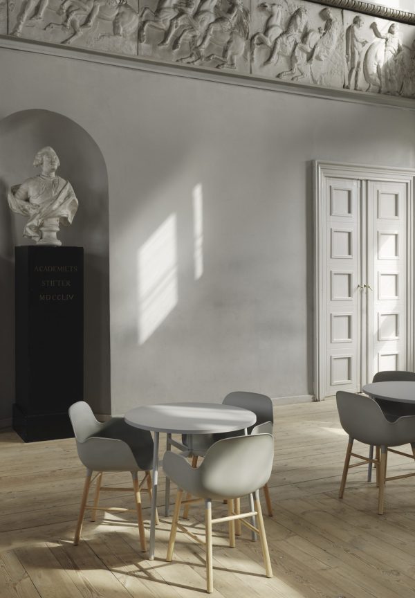Moderne minimalistisk spiseplads med grå stole og en NORMANN COPENHAGEN - Union Bord Ø80 i et rum med klassisk arkitektur, herunder en buet alkove med statue og indviklet list. stærkt sollys strømmer gennem vinduet.
