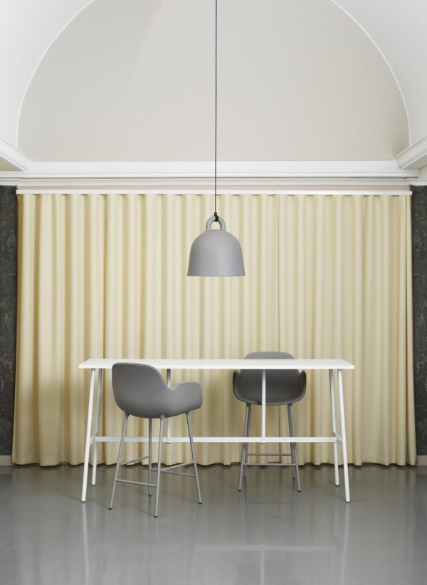 En minimalistisk spisestue med et hvidt bord og to grå stole, oplyst af en NORMANN COPENHAGEN - Bell Lampe Ø42, mod en baggrund af cremefarvede gardiner under et hvidt buet loft.