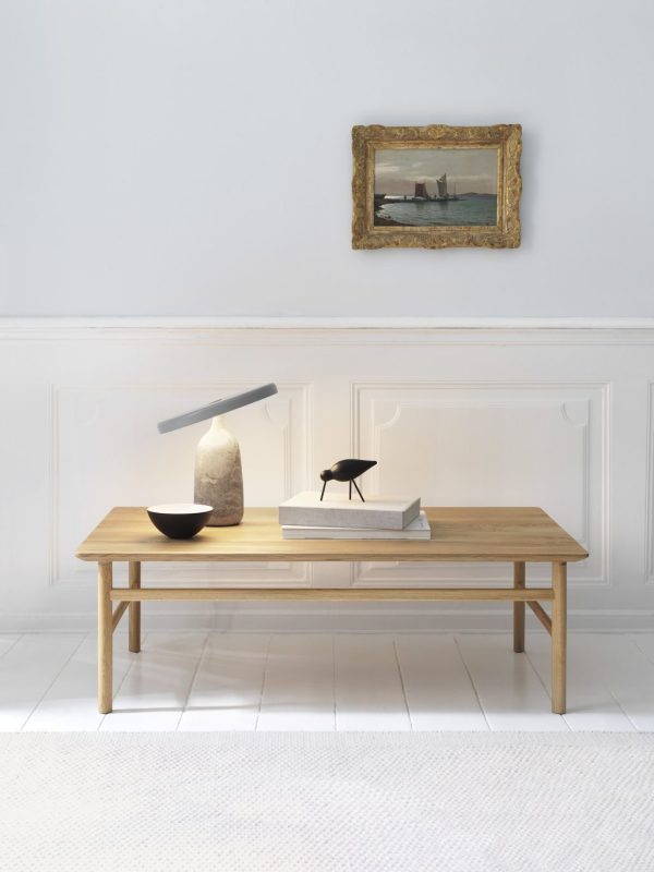 Et minimalistisk værelse med en træbænk med en stenlampe, en sort dekorativ fugl og bøger. Et indrammet maleri fra TomorrowsDesign hænger ovenover på en hvid panelvæg.