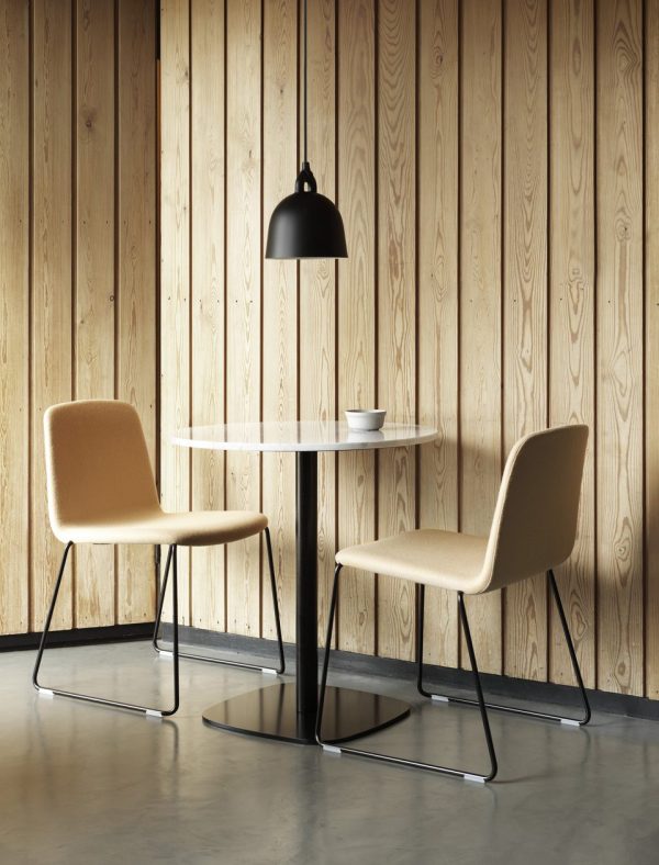Et minimalistisk caféhjørne med to solbrune polstrede stole og et hvidt rundt bord, under et sort NORMANN COPENHAGEN - Bell Lampe Ø22 lys, mod en træpanelvæg. en enkelt hvid kop står på bordet.