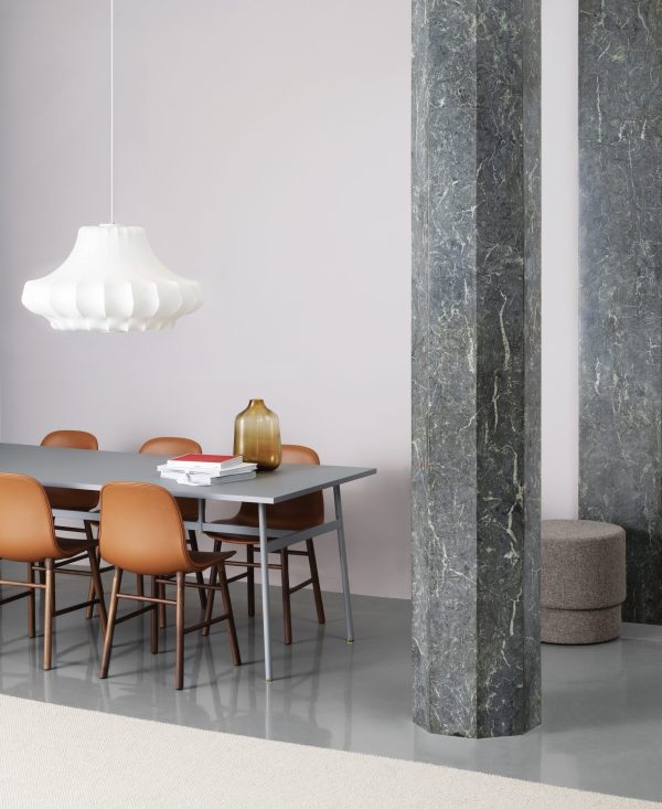 En moderne spisestue med et mørkt træbord med fire brune læderstole, omgivet af grå vægge og marmorsøjler. NORMANN COPENHAGEN - Phantom Lampe Mellem hænger over bordet.