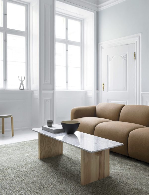 Minimalistisk stue med en NORMANN COPENHAGEN Swell Sofa 3 Pers., et sofabord med marmorplade på et tekstureret tæppe og store vinduer i et lyst, hvidt interiør.