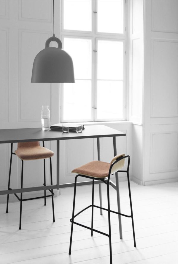Et arbejdsområde i minimalistisk stil med et elegant, sort bord med en NORMANN COPENHAGEN - Bell Lampe Ø42 overheadlampe, to taburetter med brune sæder og store hvide vinduer i et rum med hvide vægge og hvidt trægulv.