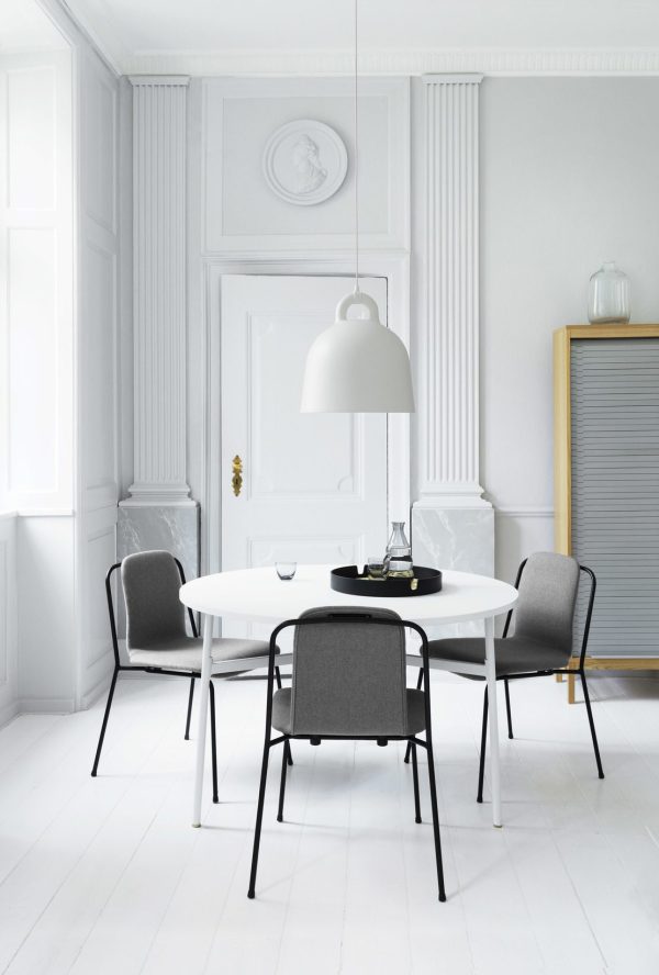 En minimalistisk spisestue med et hvidt ovalt bord og fire moderne designmøbler stole under en stor hvid pendel. Rummet har hvide panelvægge, et trægulv og et subtilt gråt skab.
