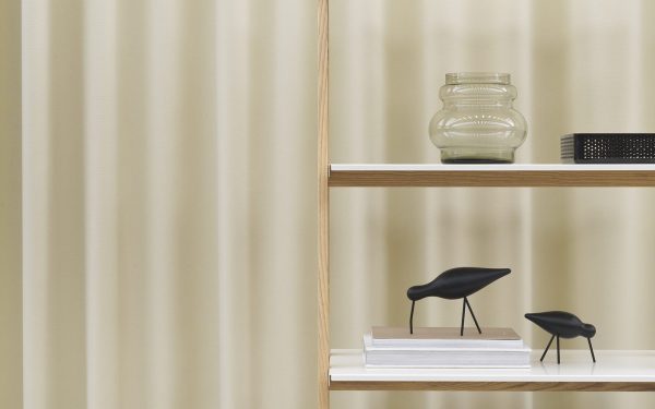 Et minimalistisk interiør med et stribet cremegardin og en NORMANN COPENHAGEN One Step Up Bogreol, der viser en glaskrukke, en stak bøger og to små sorte dekorative fuglefigurer.